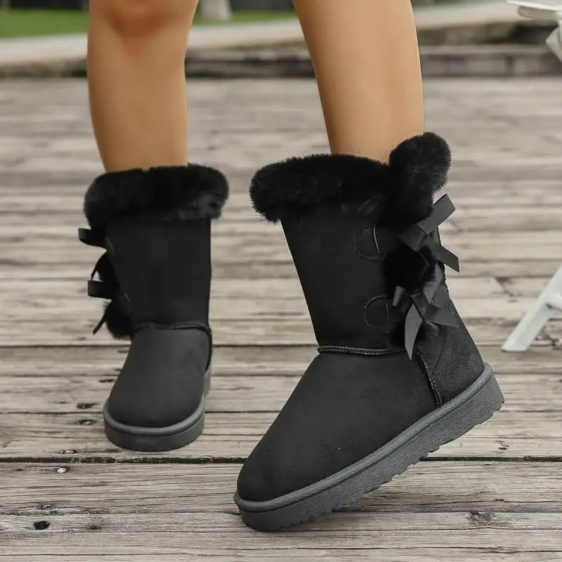Black winter boots with fur trim and bows on a wooden floor.