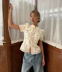 Woman wearing a lace top and jeans standing in front of a window with lace curtains.