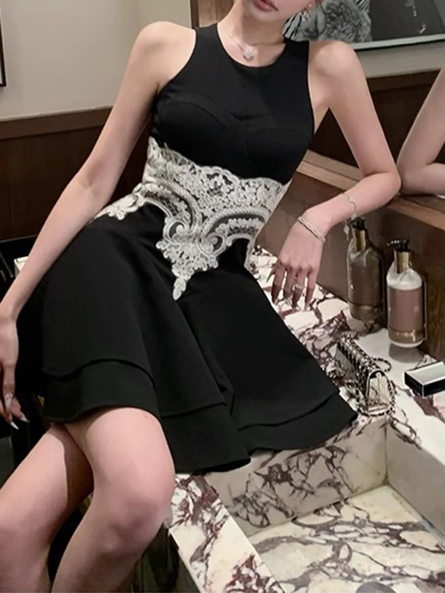Woman wearing a black dress with white lace details sitting on a chair.