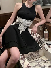 Woman wearing a black dress with white lace details sitting on a chair.