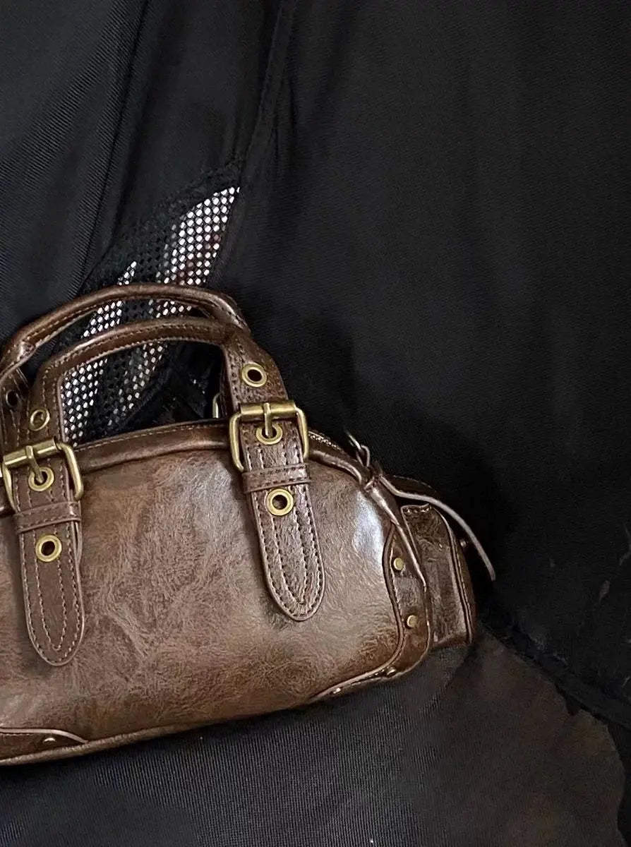 Brown leather handbag with gold buckles on a black background