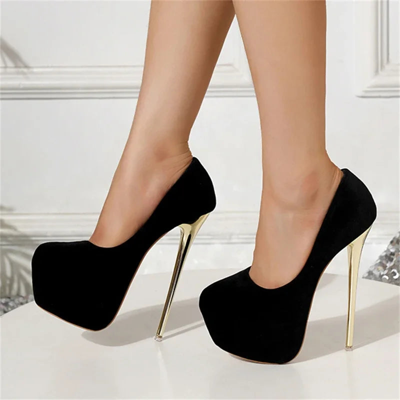 Black high-heeled shoes with gold tips worn by a person on a white background