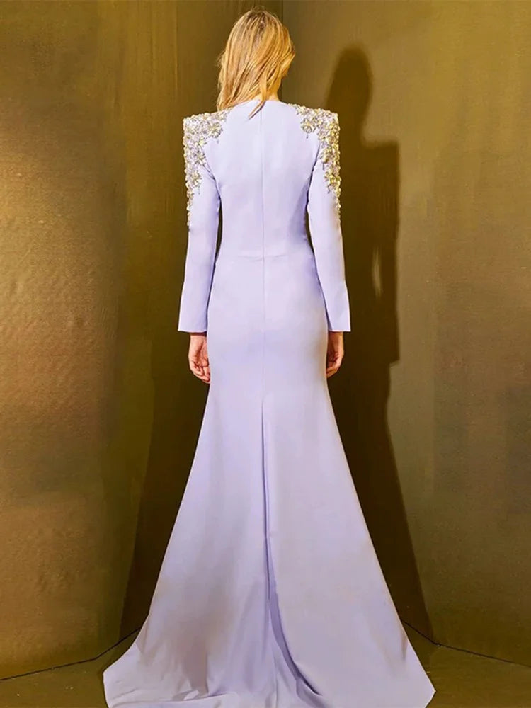 Woman wearing a light purple evening gown with embellished shoulders against a gold background