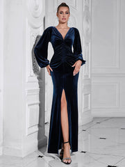 Woman wearing a dark blue velvet dress with a high slit in a white room.