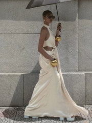 Woman in a flowing white dress holding an umbrella against a gray wall.