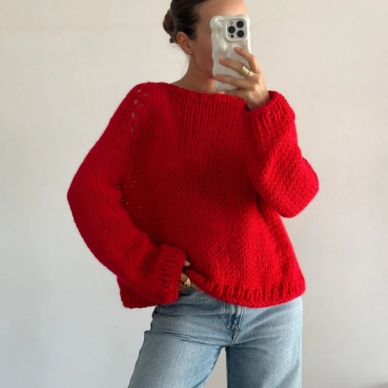 Person wearing a red sweater and light blue jeans against a plain background