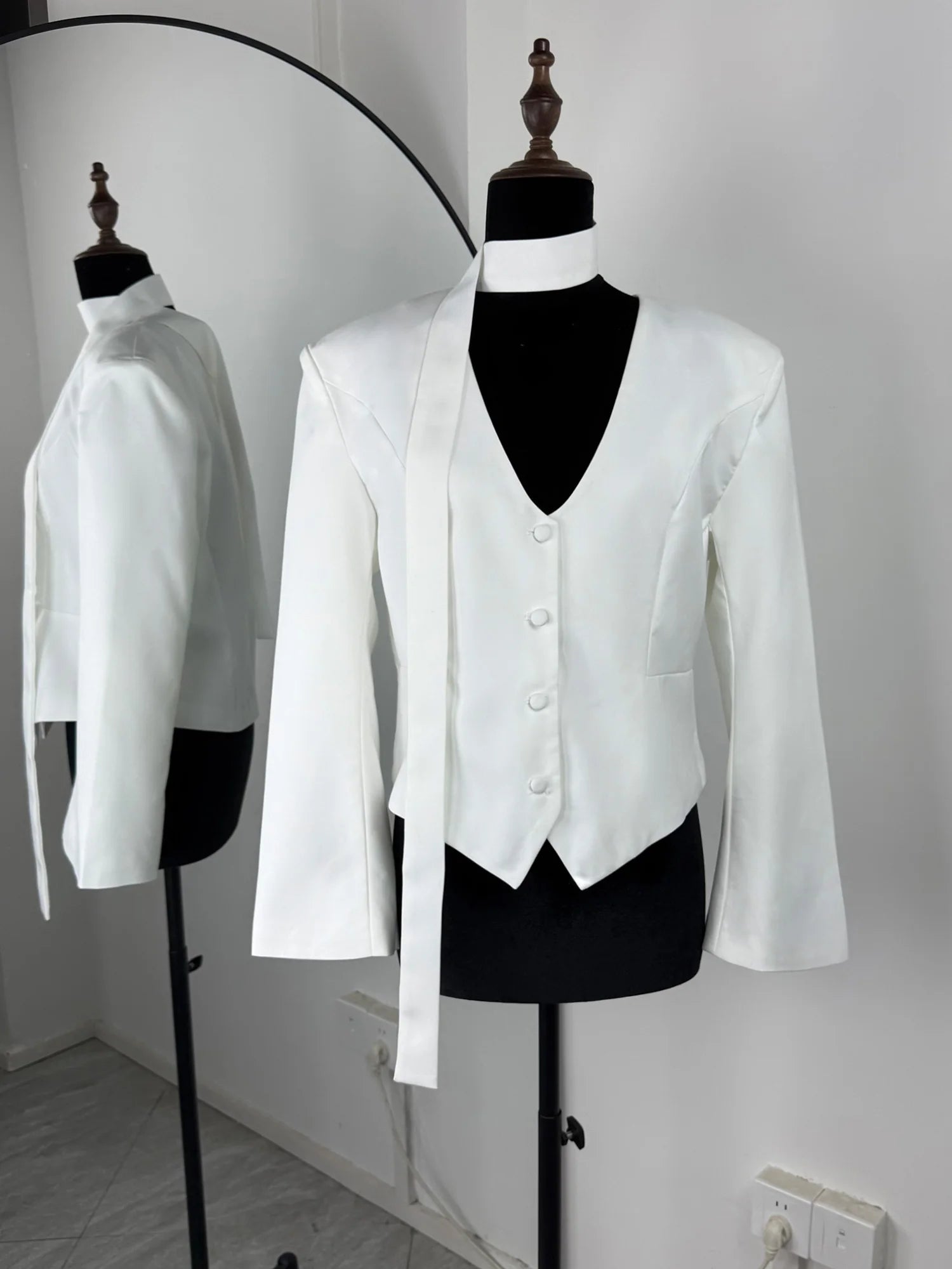 White tuxedo jacket and vest on mannequins against a white wall.
