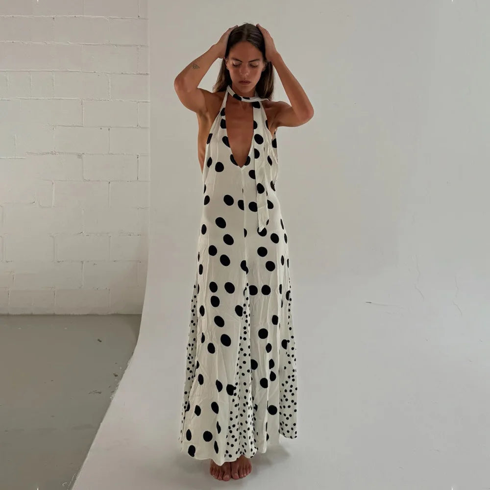 Woman wearing a long polka dot dress against a white brick wall.