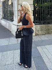 Woman in a navy polka dot dress standing on a sidewalk.