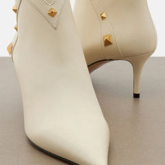 Close-up of white leather pointed toe ankle boots with gold studs, front view.