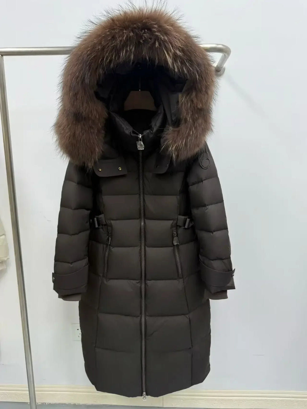 Long dark coat with fur hood on a rack against a white background