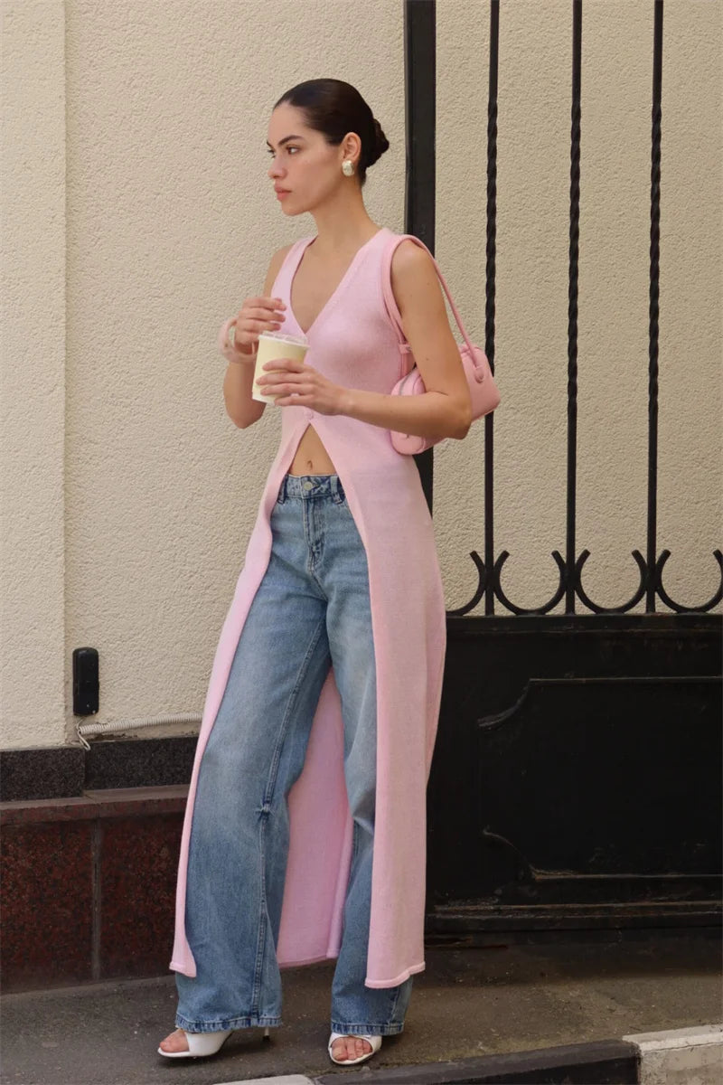 Woman in a pink cardigan and blue jeans holding a coffee cup on a street.