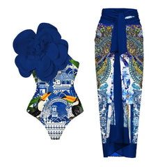 One-shoulder blue and white scenic print swimsuit with large blue floral applique and matching printed sarong.