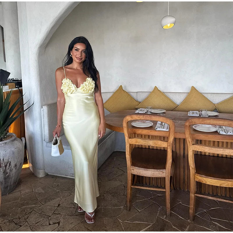 Woman in a long, light-colored dress standing in a dining area with wooden chairs and tables.