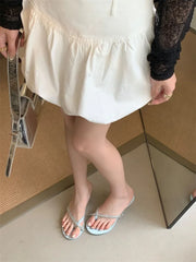Person wearing white sandals with decorative straps on a neutral background