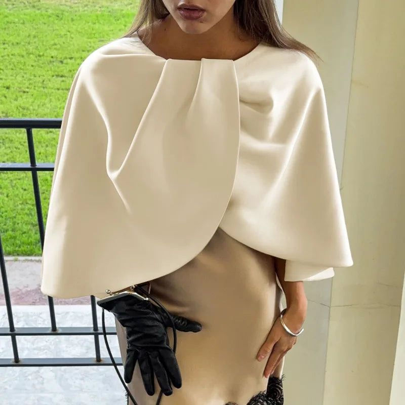 Person wearing a white cape and black gloves outdoors.