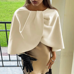 Person wearing a white cape and black gloves outdoors.