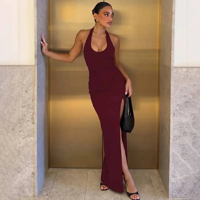 Person wearing a burgundy halter neck maxi dress with a thigh split leaning against a wall