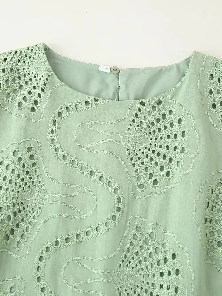 Close-up of a light green sleeveless top with intricate cut-out pattern on a white background