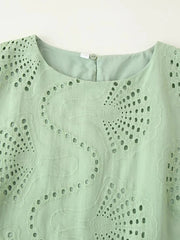 Close-up of a light green sleeveless top with intricate cut-out pattern on a white background