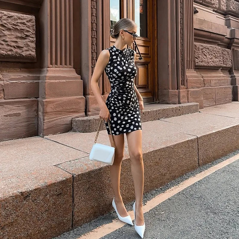 Woman in a black and white polka dot dress standing on steps in an urban setting.