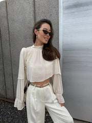 Woman wearing a white outfit with sunglasses against a gray wall.
