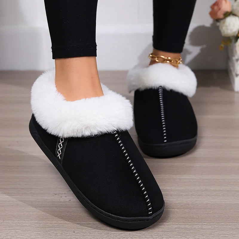 Black slippers with white fur trim worn indoors on a wooden floor.