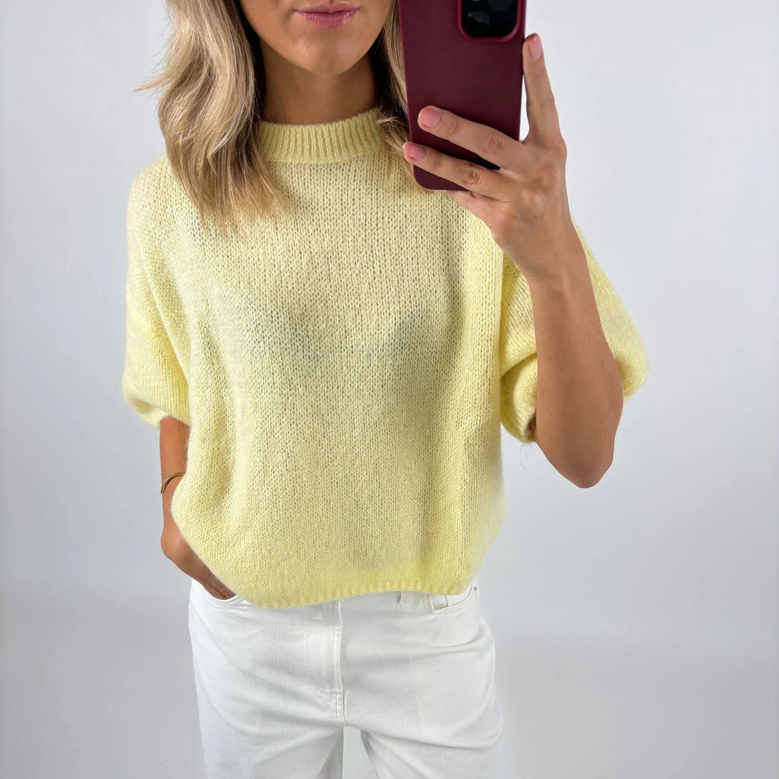 Person wearing a yellow sweater and white pants against a plain background