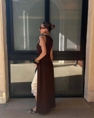 Woman in a long brown dress standing in front of a large window.