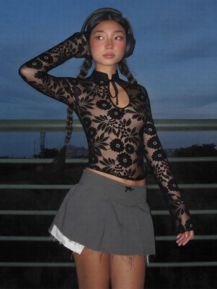 Person wearing a black lace top and gray pleated skirt against a dark background
