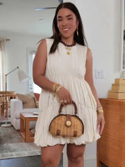 Woman in a white dress holding a wicker handbag in a living room.
