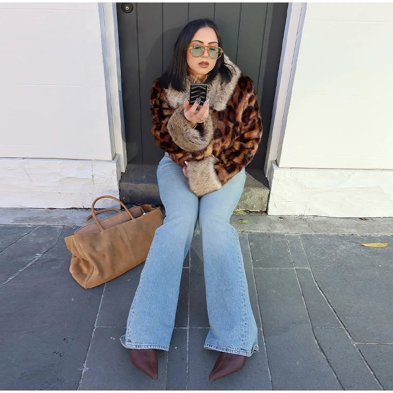 Woman in a leopard print jacket and blue jeans sitting on a step outdoors.