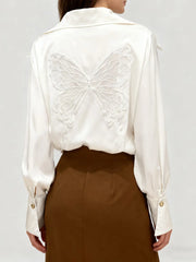 White blouse with butterfly embroidery on a plain background