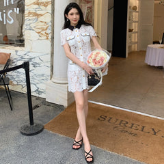 Woman in a white lace dress holding flowers outside a building with 'SURELY Casa' doormat.