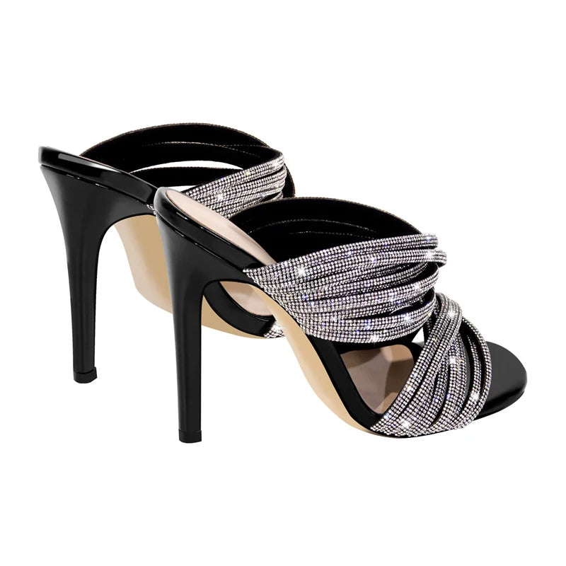 Close-up view of black patent leather mule sandals showcasing the crystal-embellished twisted straps.