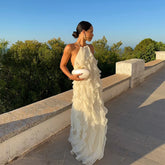 Woman in a white ruffled dress standing on a stone pathway with greenery in the background
