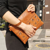Person holding a brown leather clutch with grommet details on a city street.