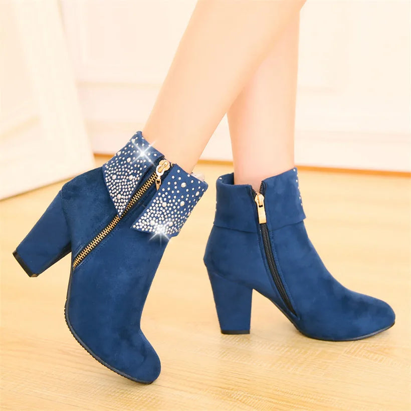 Blue ankle boots with gold zippers worn by a person on a wooden floor.