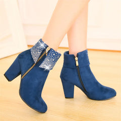 Blue ankle boots with gold zippers worn by a person on a wooden floor.