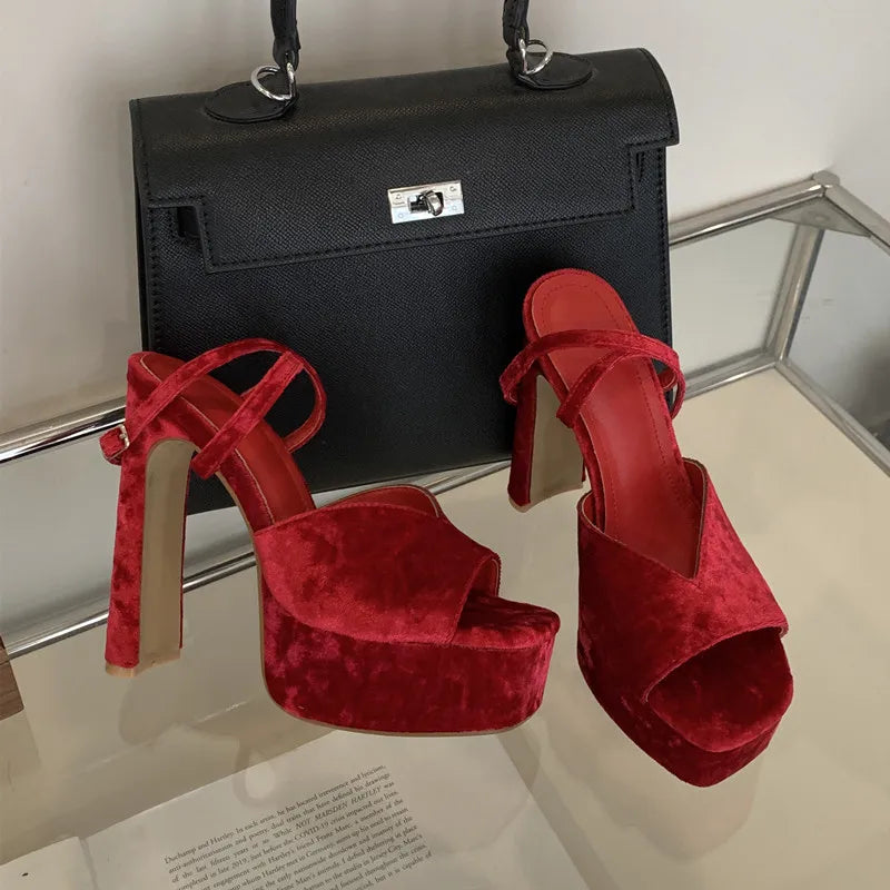 Red high-heeled shoes and a black handbag on a reflective surface.
