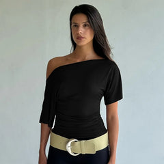 Woman wearing a black one-shoulder top with a beige belt against a plain background
