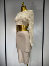 Mannequin wearing a white beaded top and beige skirt against a gray background