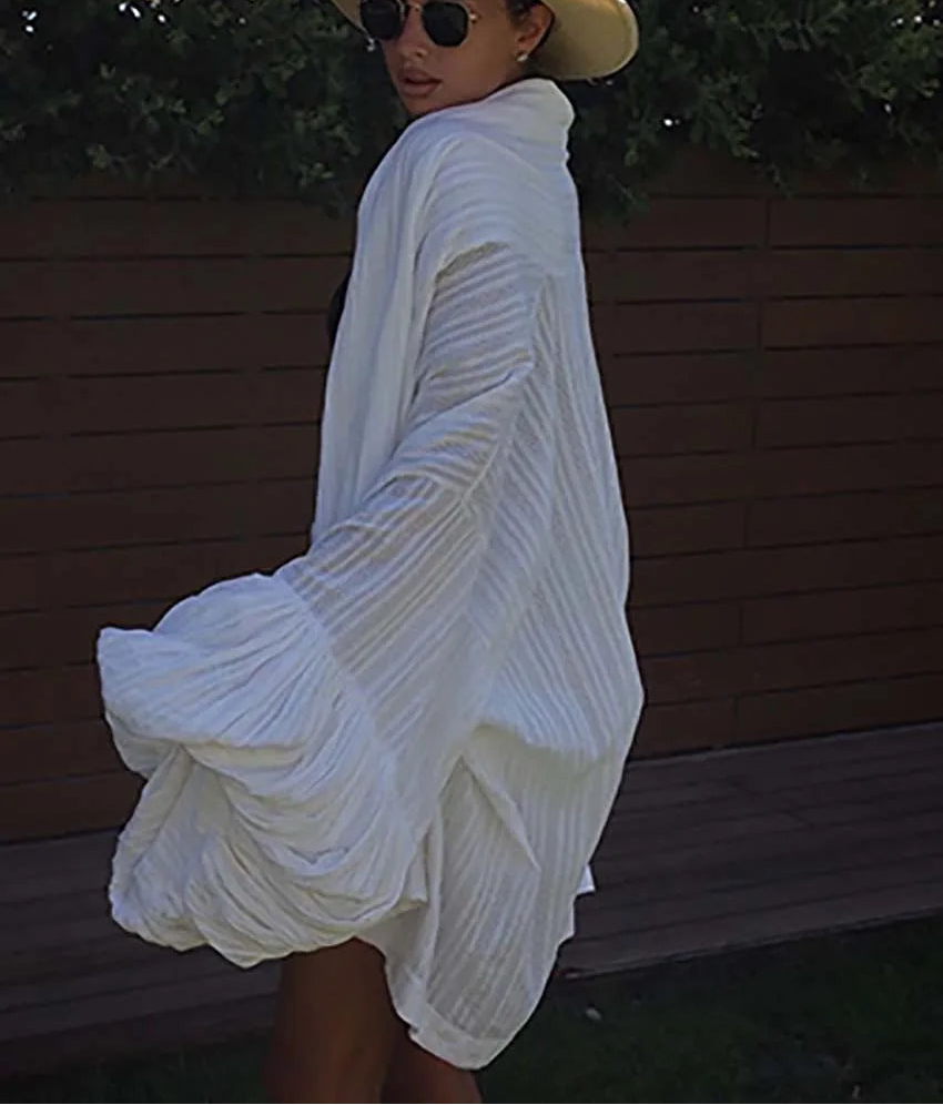 Person wearing a white dress and straw hat with sunglasses, standing against a wooden wall.
