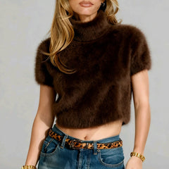 Woman wearing a brown fur top and blue jeans with a leopard print belt against a gray background