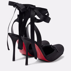 Black high-heeled shoes with red soles and black ribbons on a light gray background