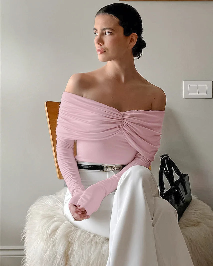 Woman wearing a pink off-shoulder top and white pants sitting on a chair.