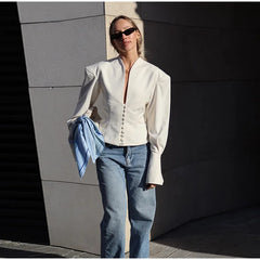 Woman wearing a white blouse and blue jeans against a gray wall.