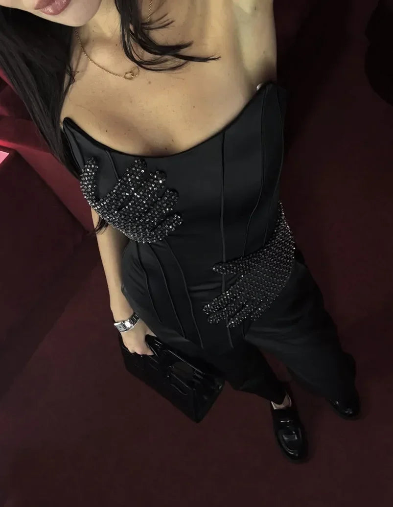 Person wearing a black dress with embellishments on a dark background
