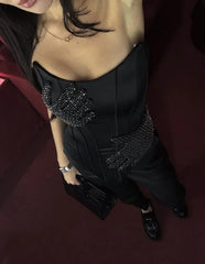 Person wearing a black dress with embellishments on a dark background