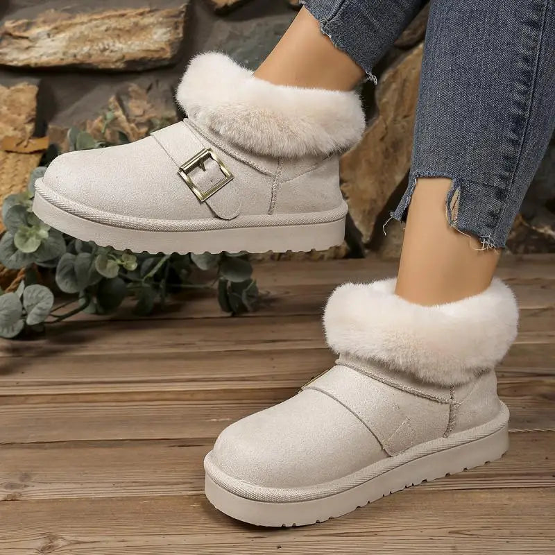 White winter boots with fur trim worn by a person on a wooden floor.